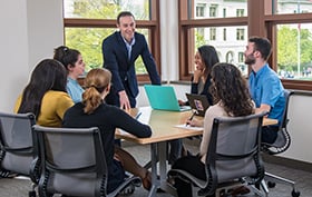 Students seated at a table looking at a man standing at the table