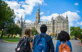 Three students with backpacks looking at a building on the Georgetown campus