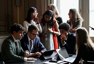 Students huddled around laptops, four seated and four standing